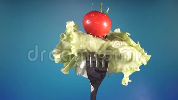 用新鲜的红番茄和黄瓜拌叉放在水滴里生菜以蓝色为背景旋转视频的预览图