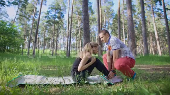 快乐的夫妻在草地上的公园里做体育锻炼一个女人在摇报一个男人帮她视频的预览图