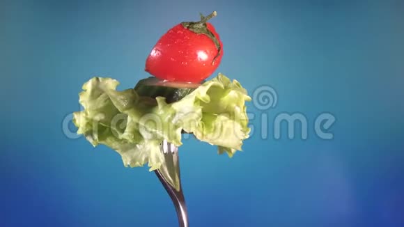 用新鲜的红切番茄和黄瓜叉在水滴和生菜中旋转蓝色背景视频的预览图