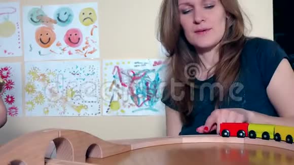 妈妈和她可爱的小女孩在家里的桌子上玩木玩具火车视频的预览图