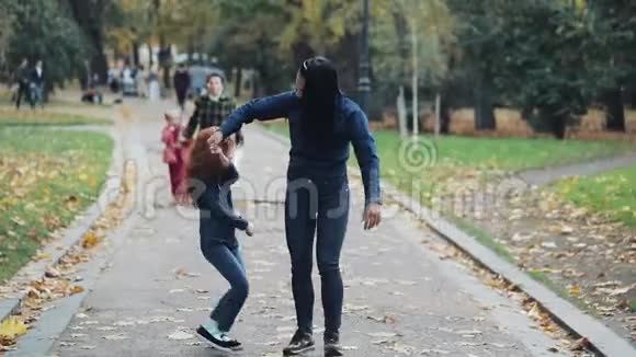 快乐的母亲和她的小女儿在秋天公园玩得很开心年轻的一家人走着笑着慢动作视频的预览图