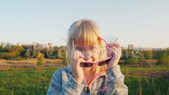 穿着运动服和太阳镜的酷女孩的肖像在镜头中轻拍微笑展示体操动作视频的预览图