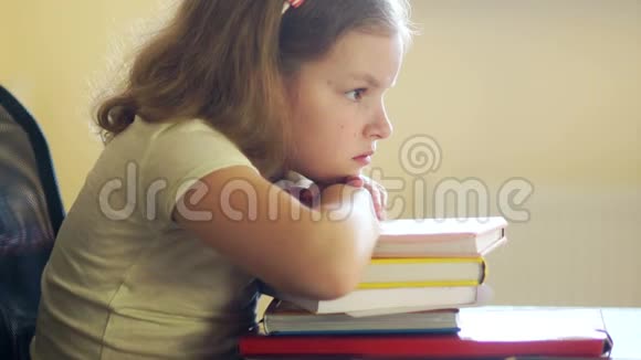 悲伤的女孩坐在桌子旁拿着一堆书学校教育的问题回到学校视频的预览图