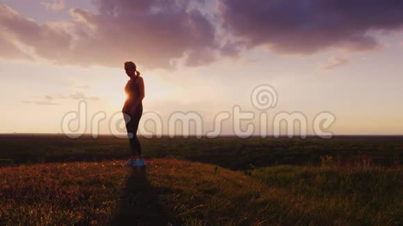日落时一个女人正在风景如画的地方做运动在天空和绿色平原的背景下在视频的预览图