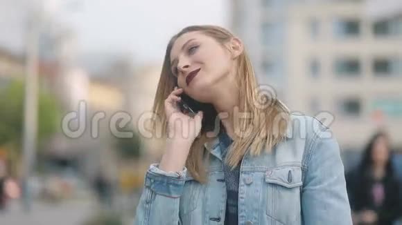 在熙熙攘攘的街道中间一个红唇在电话中说话的迷人女人的肖像视频的预览图