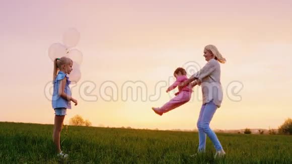一个快乐的母亲两个女孩在日落时和他们一起玩一个打开双手二女儿看着她视频的预览图