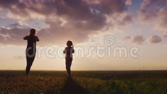 一个年轻女子的剪影有个孩子在大自然中做健身日落时风景如画的地方4K慢动作视频视频的预览图