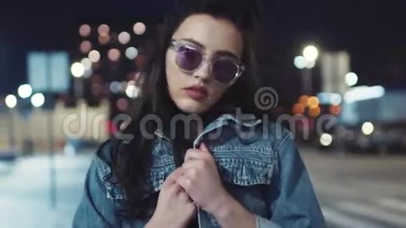 漂亮的年轻性感的黑发女孩穿着牛仔裤夹克和时尚的太阳镜在相机旁边摆姿势迷人的外表时尚视频的预览图
