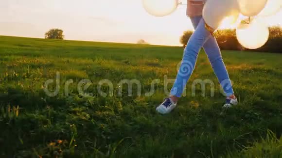 一个年轻的女人带着气球在绿色的草地上快乐地散步在镜框里有看得见的腿和球视频的预览图