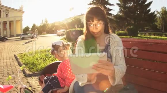 日落时分慢动作的妈妈和女儿正坐在路边的长凳上视频的预览图