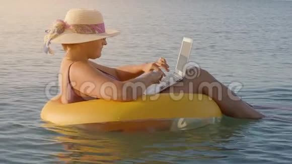 女性自由职业者在一台笔记本电脑上工作坐在海里的充气戒指里视频的预览图
