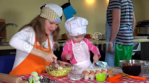 可爱的小女孩戴着厨师帽她年轻的父母准备饼干视频的预览图