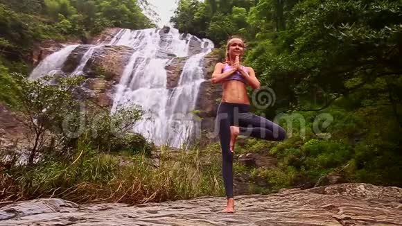 女孩站在瑜伽的位置在平坦的石头瀑布视频的预览图