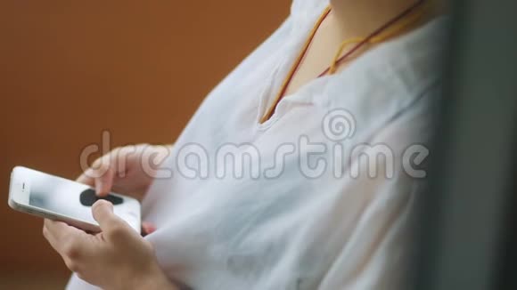 年轻温柔的女人穿着白色透明衬衫纹身在木制背景下使用智能手机视频的预览图