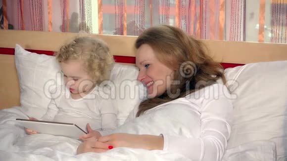 漂亮的妈妈睡着了女儿在床上玩平板电脑视频的预览图