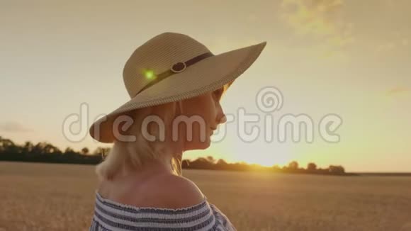 一个戴帽子的年轻女子看着麦田上空的夕阳背面视频的预览图