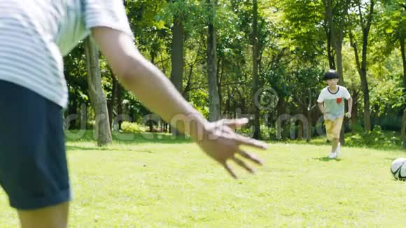 一个亚洲男孩在夏天慢动作地把足球踢向作为守门员的父亲视频的预览图