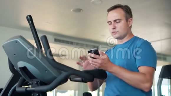 帅哥适合在健身房做运动的年轻人使用智能手机与朋友交流视频的预览图