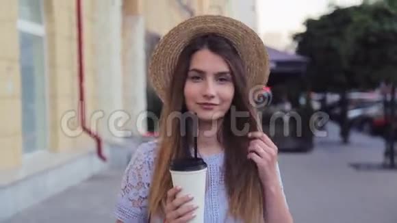 戴着夏帽的漂亮女孩拿着纸杯走在小巷里视频的预览图