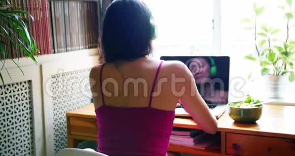 女性在使用笔记本电脑时听歌的后视图视频的预览图