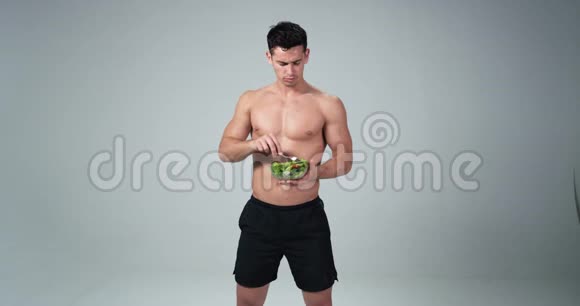 一个男性健身模特拿着塑料碗在白色背景上吃新鲜沙拉他微笑着为了健康的生活视频的预览图