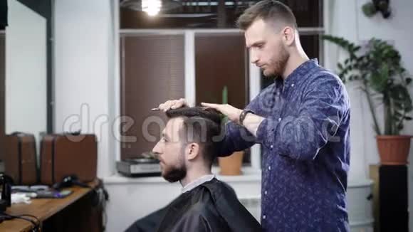 一位时尚的理发师轻轻地给他客户梳头以便在一家美容院为他创造一个时尚的发型视频的预览图