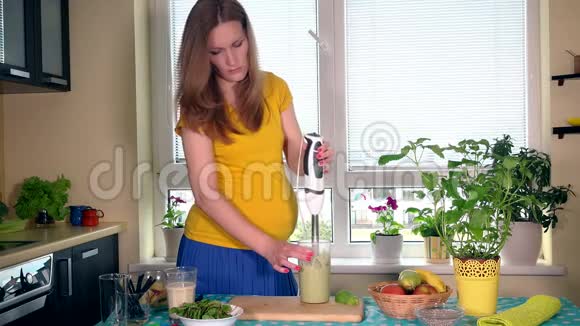 孕妇在厨房用搅拌机搅拌牛奶和天然水果视频的预览图