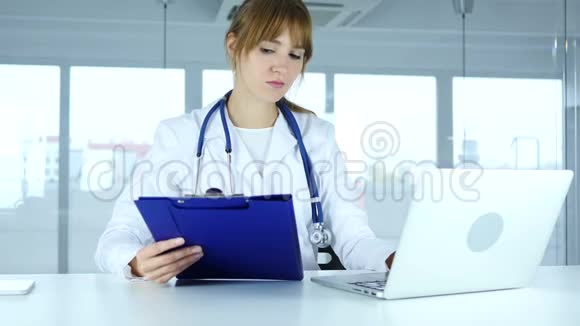 年轻女医生阅读医疗报告和手提电脑视频的预览图