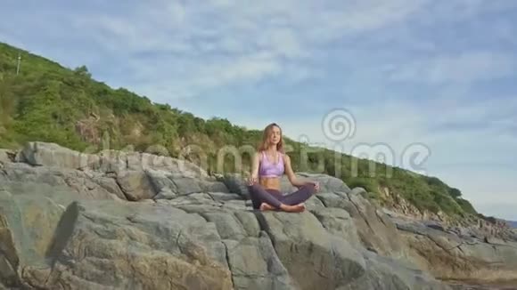 FlyCam从放松瑜伽姿势的女孩移除岩石边缘视频的预览图