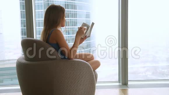 迷人的女人坐在扶手椅上看书喝咖啡茶视频的预览图