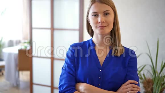 穿着深蓝色上衣的年轻美女站在客厅微笑的双臂交叉的画像视频的预览图