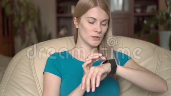 美丽迷人的女人坐在家里的椅子上用她的黑色智能手表口述信息视频的预览图