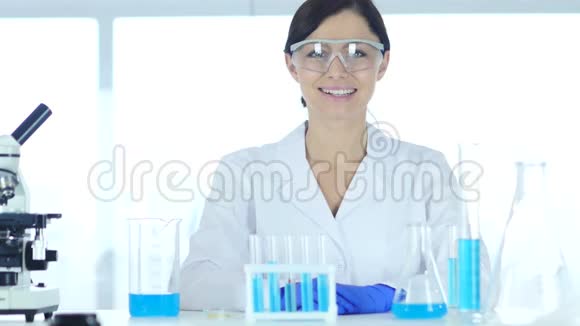 微笑成功的女科学家坐在实验室里看着摄像机视频的预览图