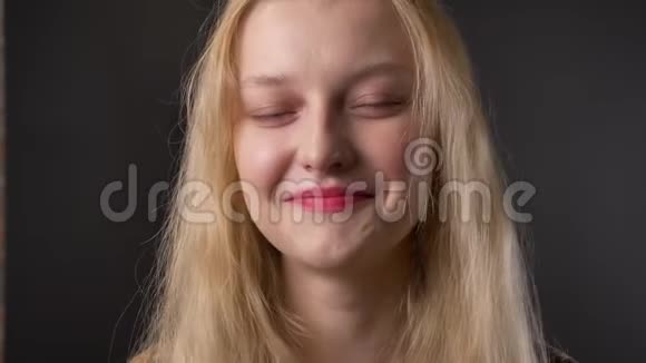 年轻可爱的金发女孩带着粉红色的口红在镜头前看着微笑着灰色的背景视频的预览图