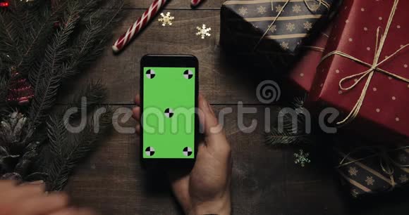 男性手在带有绿色屏幕的黑色智能手机上点击页面铬钥匙上景垂直位置圣诞节视频的预览图