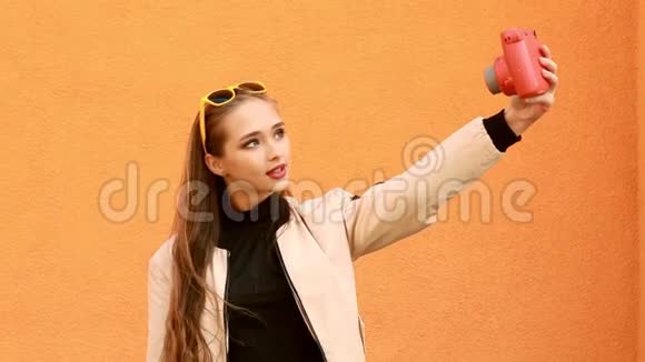 美丽的时髦女孩通过即时相机自拍橙色背景室外视频的预览图