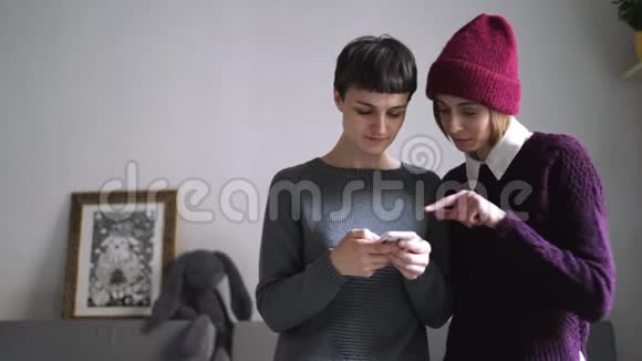 两个年轻的女人看着手机的照片使用智能手机的女性朋友视频的预览图