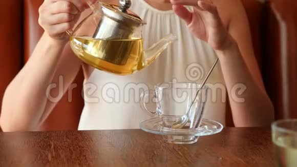 女孩把透明茶壶里的绿茶倒进透明的杯子里4K慢动作视频的预览图