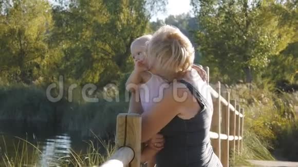 中祖母抱着她的金发女孩站在天然公园的木桥上视频的预览图