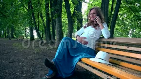 快乐的孕妇坐在长凳上打电话女性中风视频的预览图