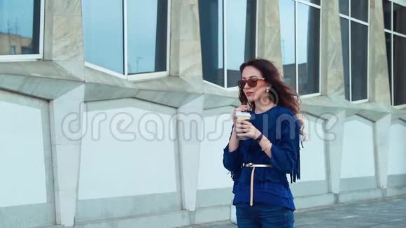 在现代城市建筑附近的街道上喝咖啡的年轻女子视频的预览图