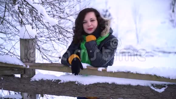 冬天森林里的年轻漂亮女孩看着相机笑着那个女孩站在木栅栏附近她是视频的预览图