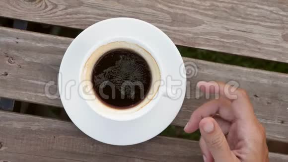 从上面看年轻人从木桌上拿着一杯美式热咖啡4K慢动作关闭视频的预览图