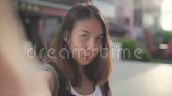 开朗美丽的年轻亚洲背包客博主女士在北京唐人街旅行时使用智能手机自拍视频的预览图