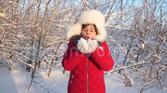 快乐的女孩在日落时吹雪花在冬天的公园里微笑小女孩用手吹雪花在视频的预览图