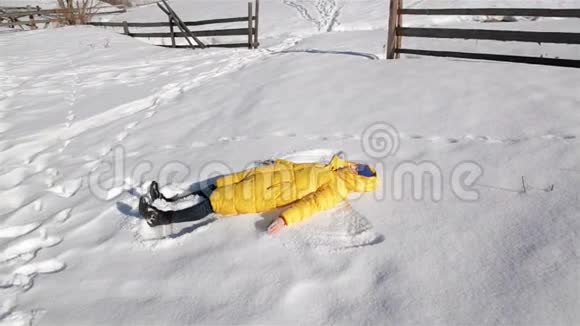 欢乐的女人正在玩冬季游戏黄夹克里的女孩躺在地上让雪天使拥有视频的预览图