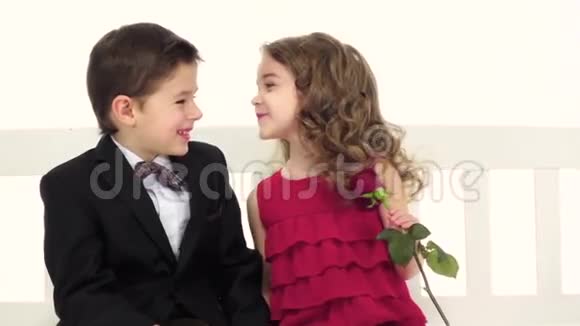 孩子们坐在秋千上聊天在女孩手一朵玫瑰白色背景慢动作关门视频的预览图