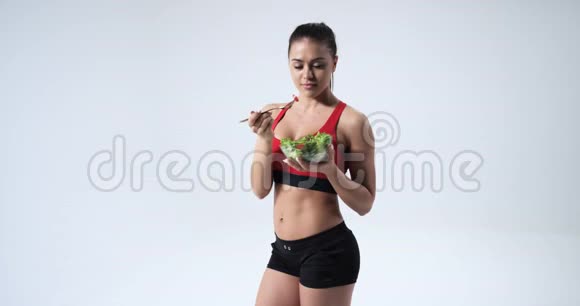 运动健身年轻女孩吃蔬菜沙拉和微笑健康的生活方式概念白色背景4k视频的预览图