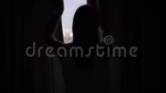 女人揭开窗帘的剪影看着窗外伸展着城外摩天大楼景观视频的预览图