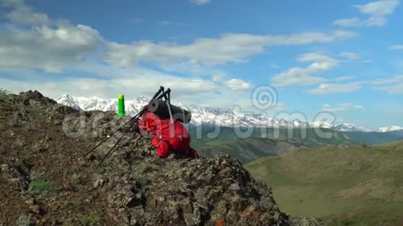 旅行者的红色背包躺在岩石上用于追踪的棍子有一个热水瓶视频的预览图